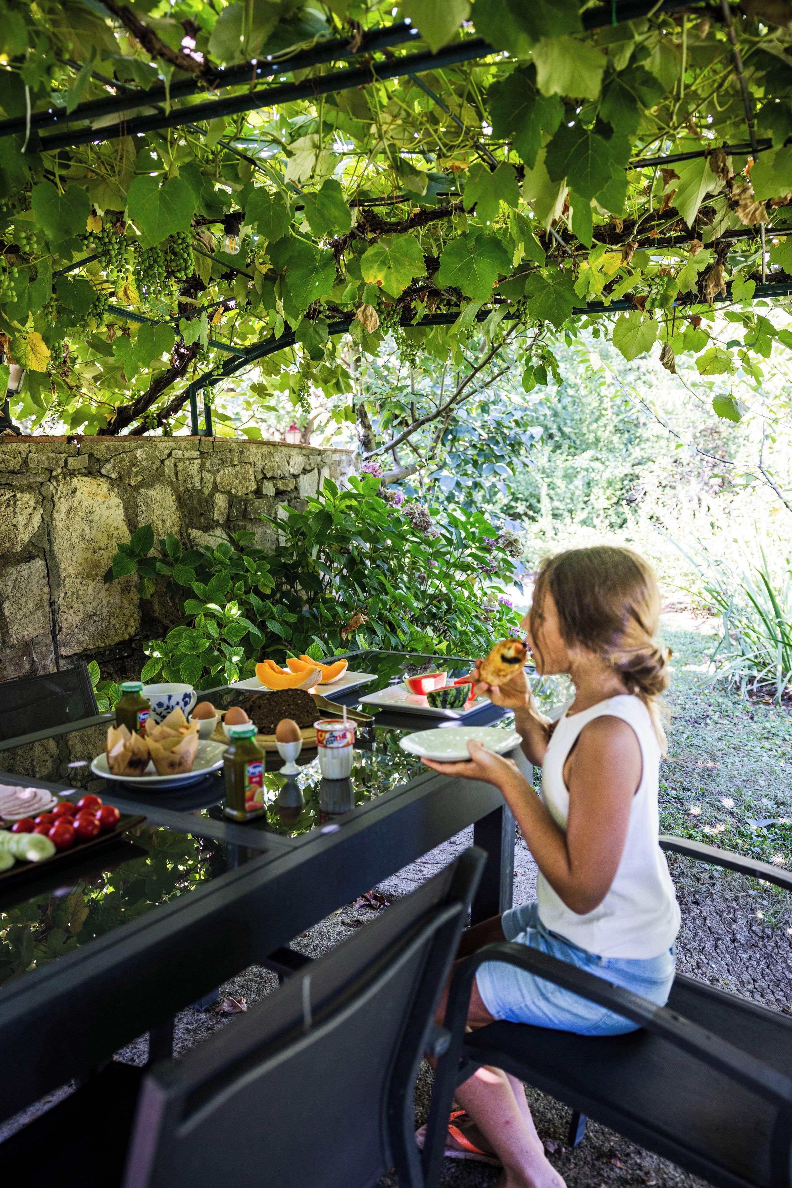 Une personne assise à une table en plein air, devant divers plats et une bouteille.