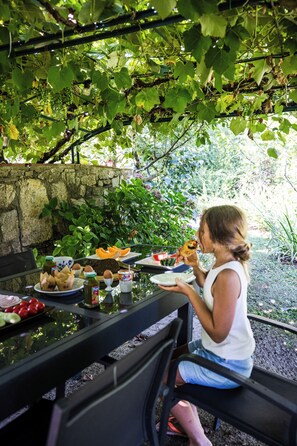 A person seated at an outdoor table with various food items and a bottle.
