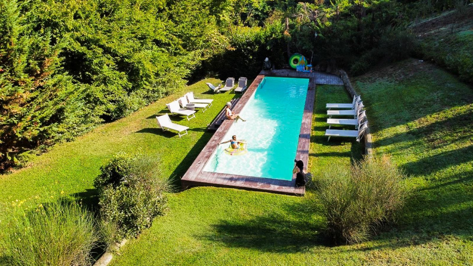 Ein rechteckiger Swimmingpool mit Holzterrasse, umgeben von weißen Liegestühlen und einer Rasenfläche.