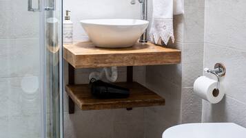 A bathroom with a glass shower enclosure, a wooden shelf with a sink, a towel rack, and a toilet.
