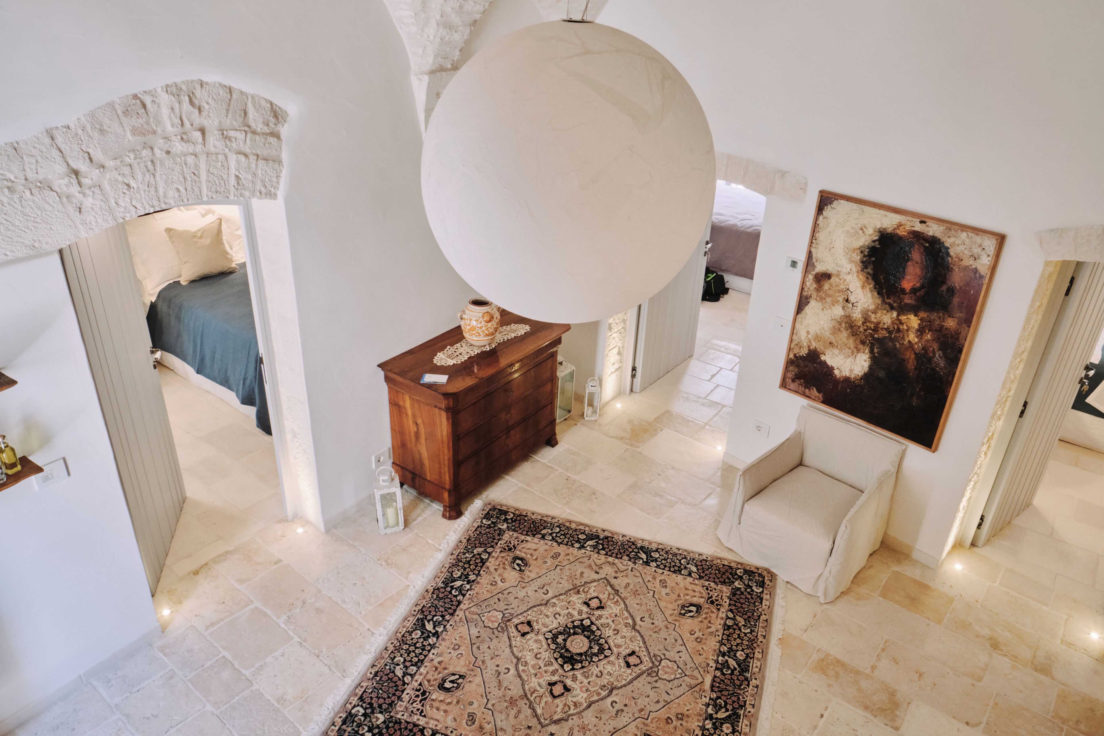 Une pièce spacieuse avec un grand lustre rond au plafond, un tapis à motifs et un tableau accroché au mur.