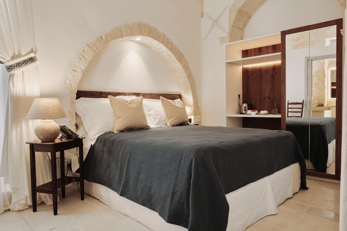 A bedroom with a bed, bedside lamp, and a mirror.
