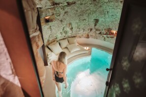 A woman in a black swimsuit standing at the edge of a hot tub with a stone wall and a beige sofa in the background. - 1783 Dimora d'Epoca (Locorotondo)