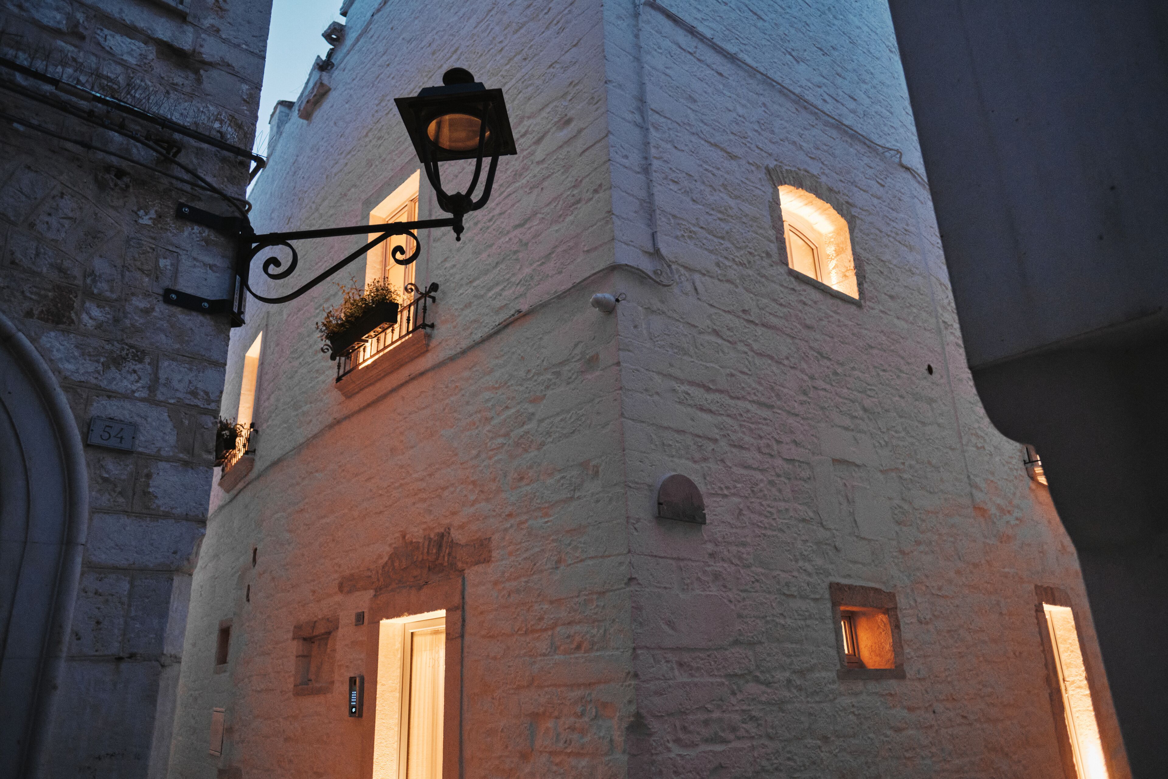 Un bâtiment historique doté d’une façade en pierre, d’un lampadaire en fer forgé et d’une petite fenêtre agrémentée d’une jardinière.