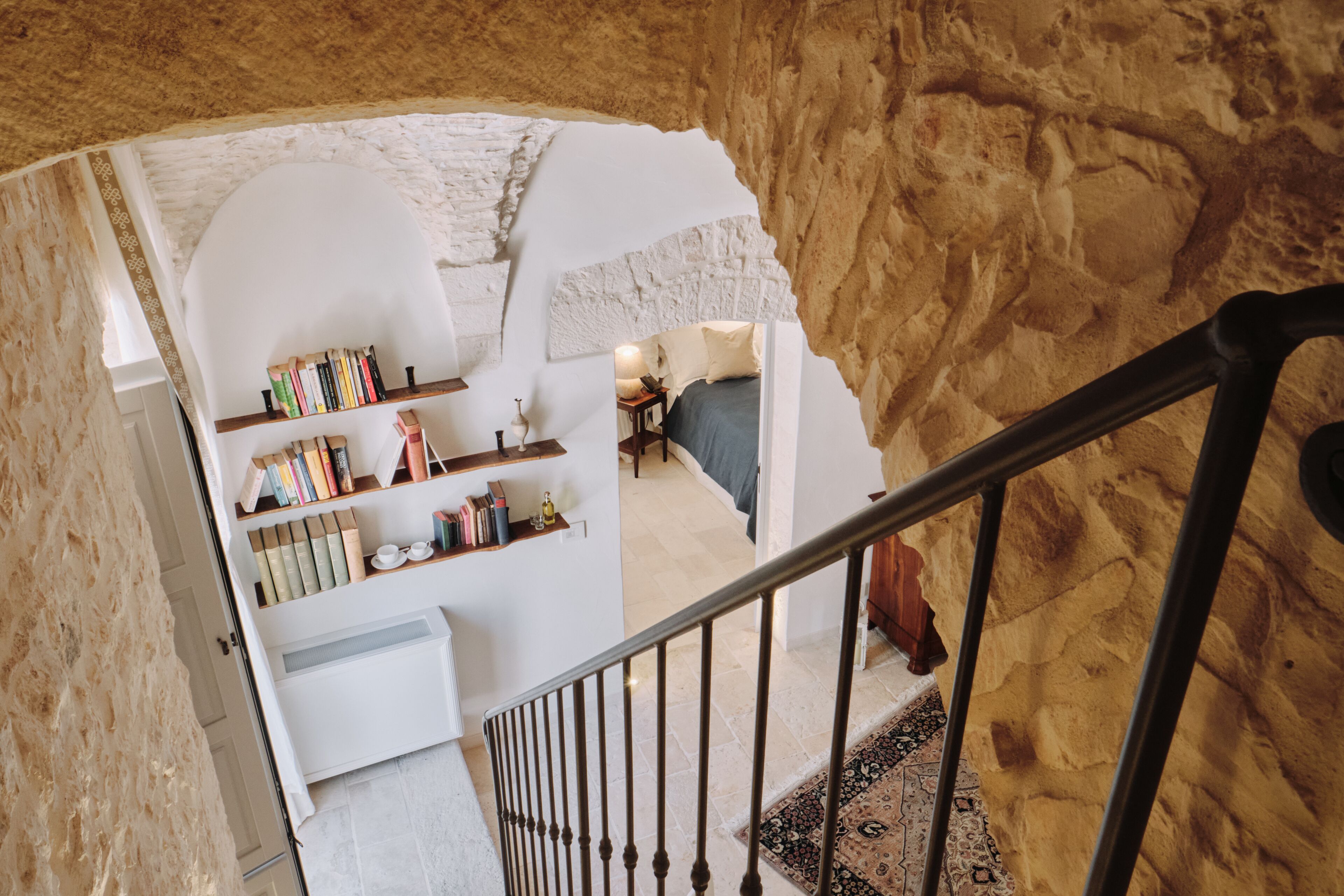 A staircase leading to a room with a stone wall, a bookshelf, and a bed.