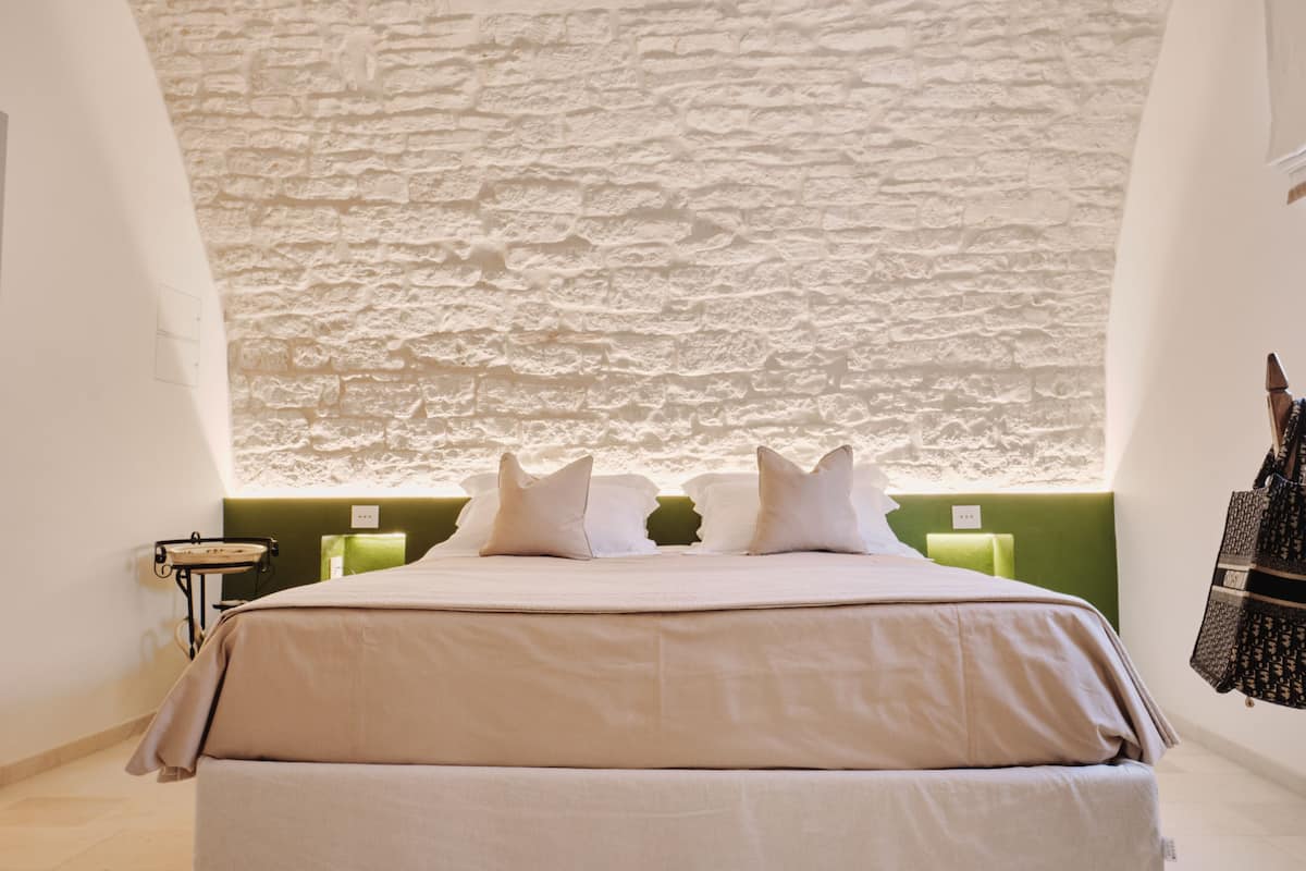 A bedroom with a stone wall, a bed with white bedding, and a green accent wall.