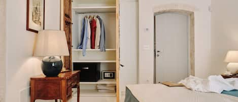 Une chambre à coucher avec un lit, une table de chevet avec une lampe, une commode en bois et une armoire où sont suspendus des vêtements.