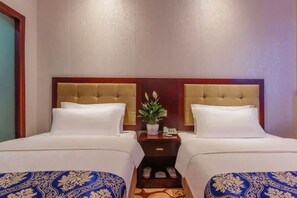 A hotel room with two beds, a nightstand with a plant, and a small drawer. - Youjia Hotel (Bijie)