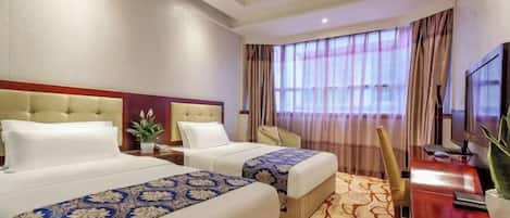 A hotel room with two beds, a desk, a chair, a TV, and a window with curtains.