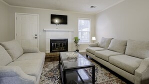 A living room with a fireplace, two sofas, a coffee table, and a television mounted on the wall. - Rosewood Townhouse (Columbia)