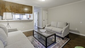 A living room with a glass coffee table, two grey sofas, a patterned rug, and a kitchen area with a stove and cabinets. - Rosewood Townhouse (Columbia)