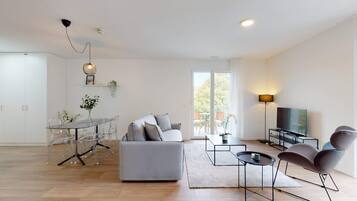 A modern living room with a grey sofa, a glass dining table, and a TV.
