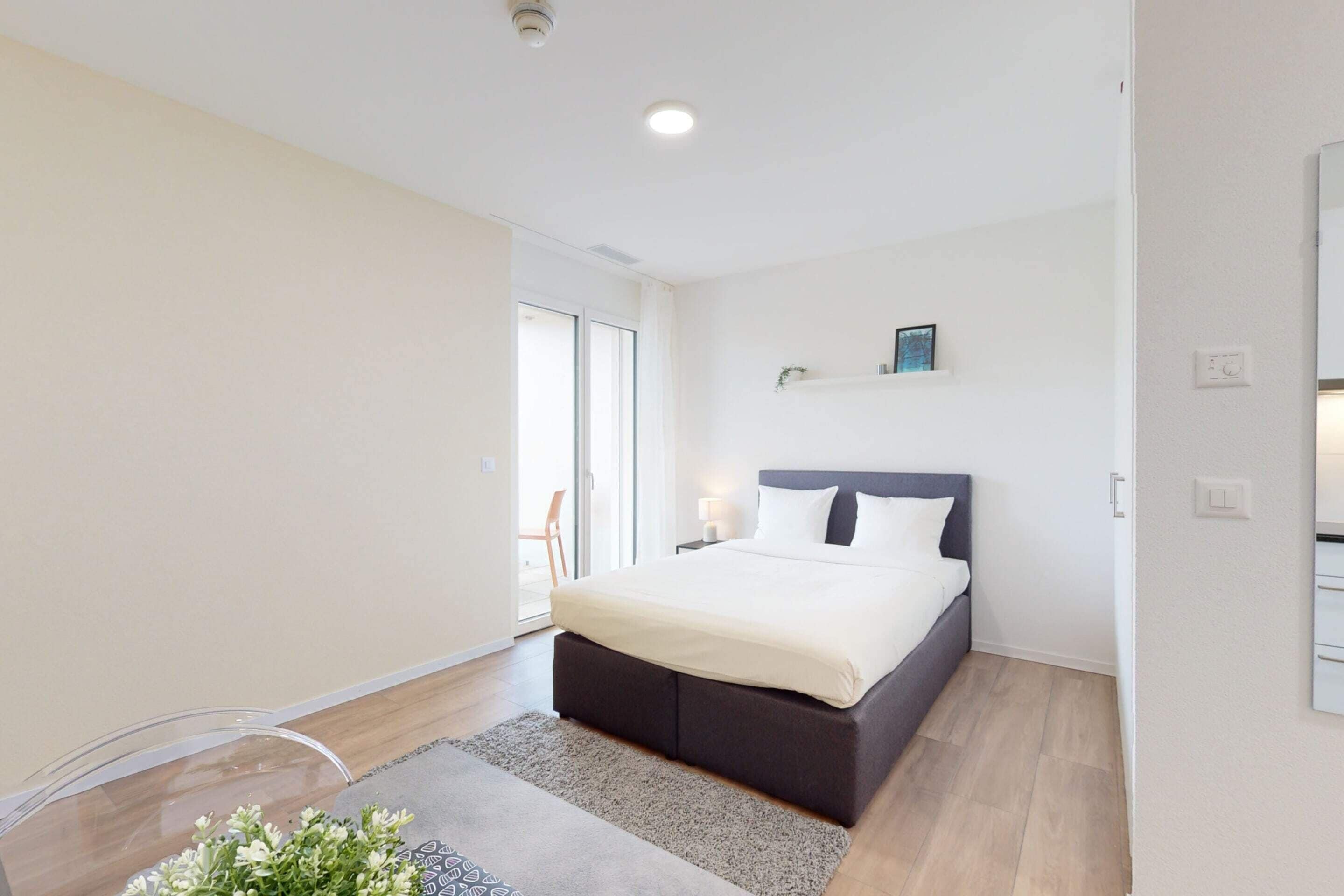 Quarto moderno com uma cama grande, uma pequena mesa de cabeceira e uma cadeira de vidro transparente.