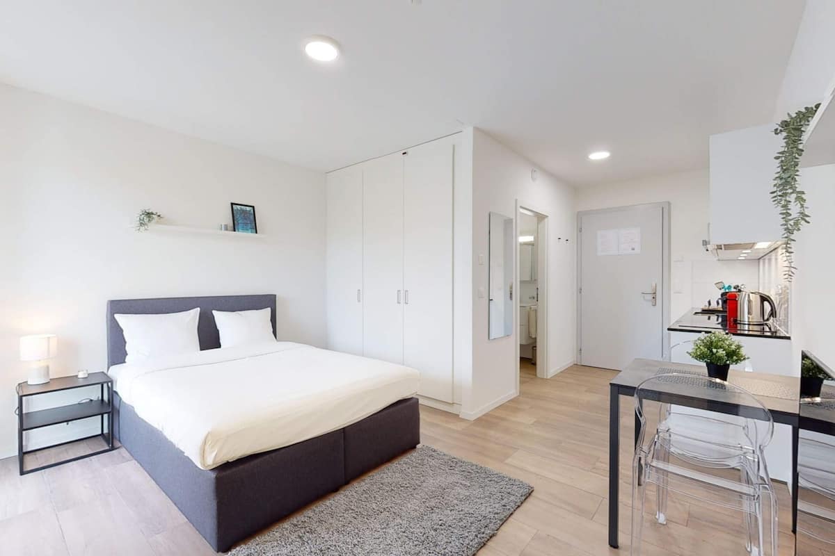 A modern bedroom with a bed, bedside table, and a small desk with a chair.