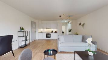 A modern living room with a grey sofa, a black coffee table, and a white orchid on the table. A black chair is visible in the foreground.