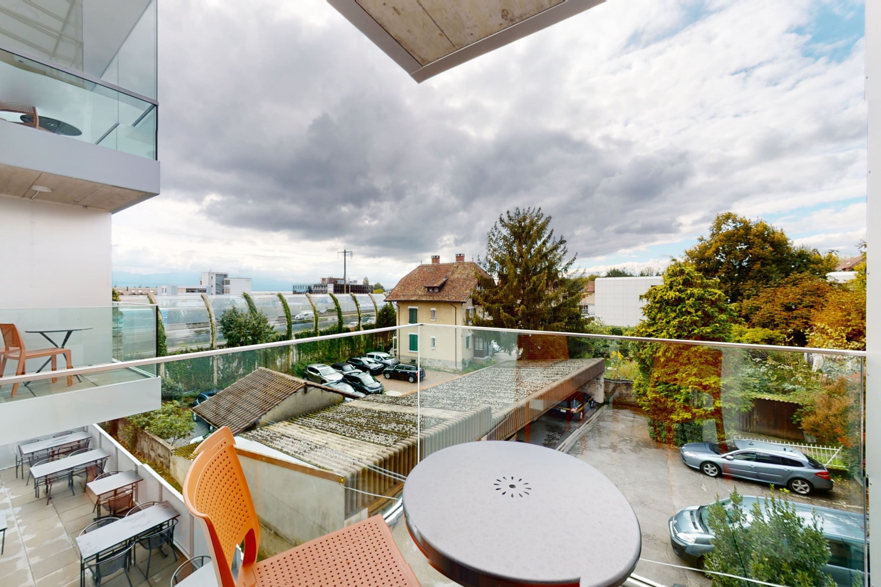 Un balcone moderno con ringhiera in vetro, arredi da esterno e vista sulla città.