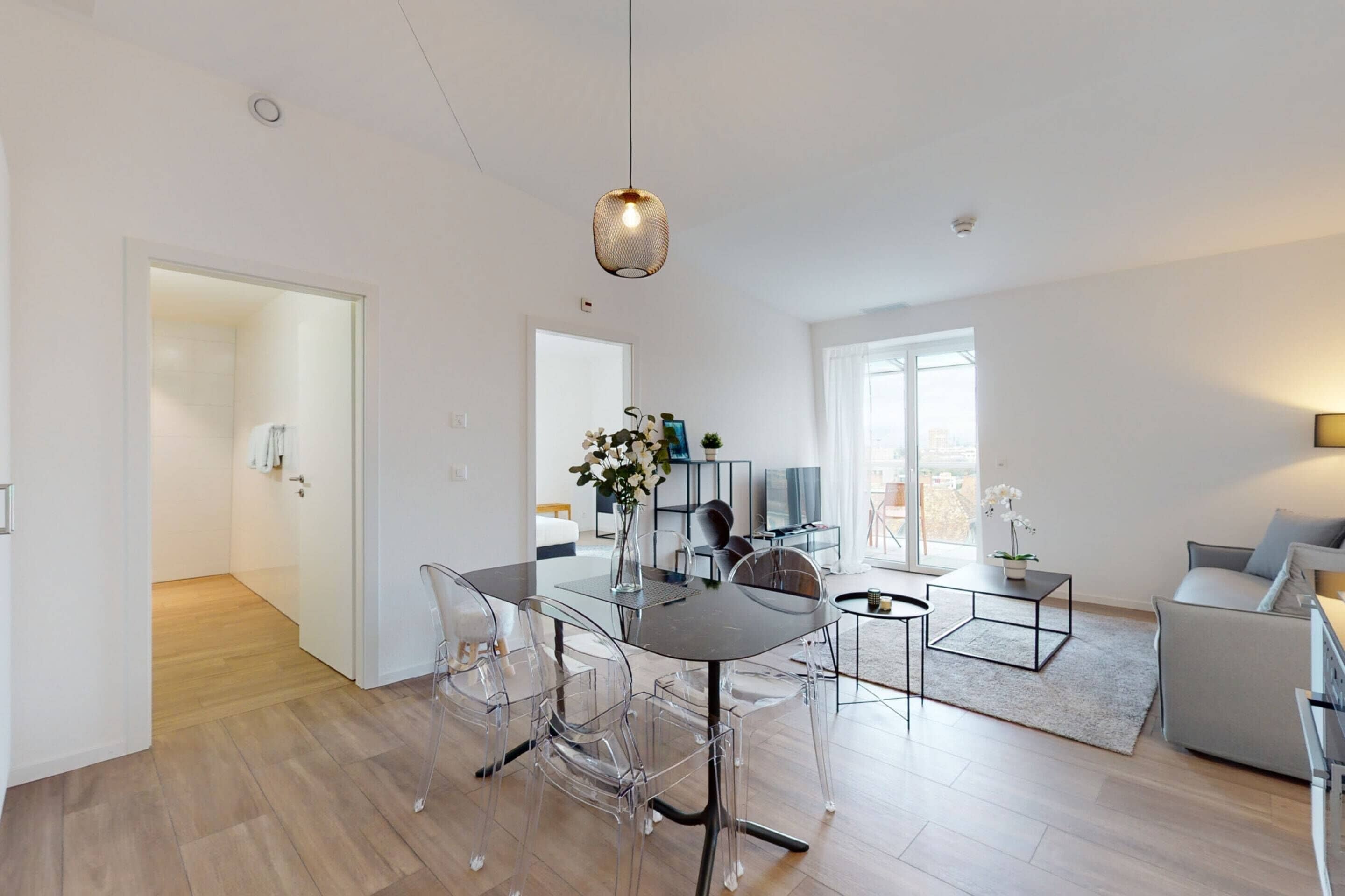 Een moderne woonkamer met een glazen eettafel, transparante stoelen, een bank en een televisie.
