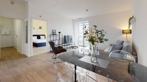A modern living room with a dining area, a sofa, a TV, and a plant. - Lodges Hotel Morges (Morges)