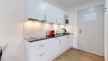 A modern kitchen with white cabinets, a black countertop, and a stainless steel kettle.