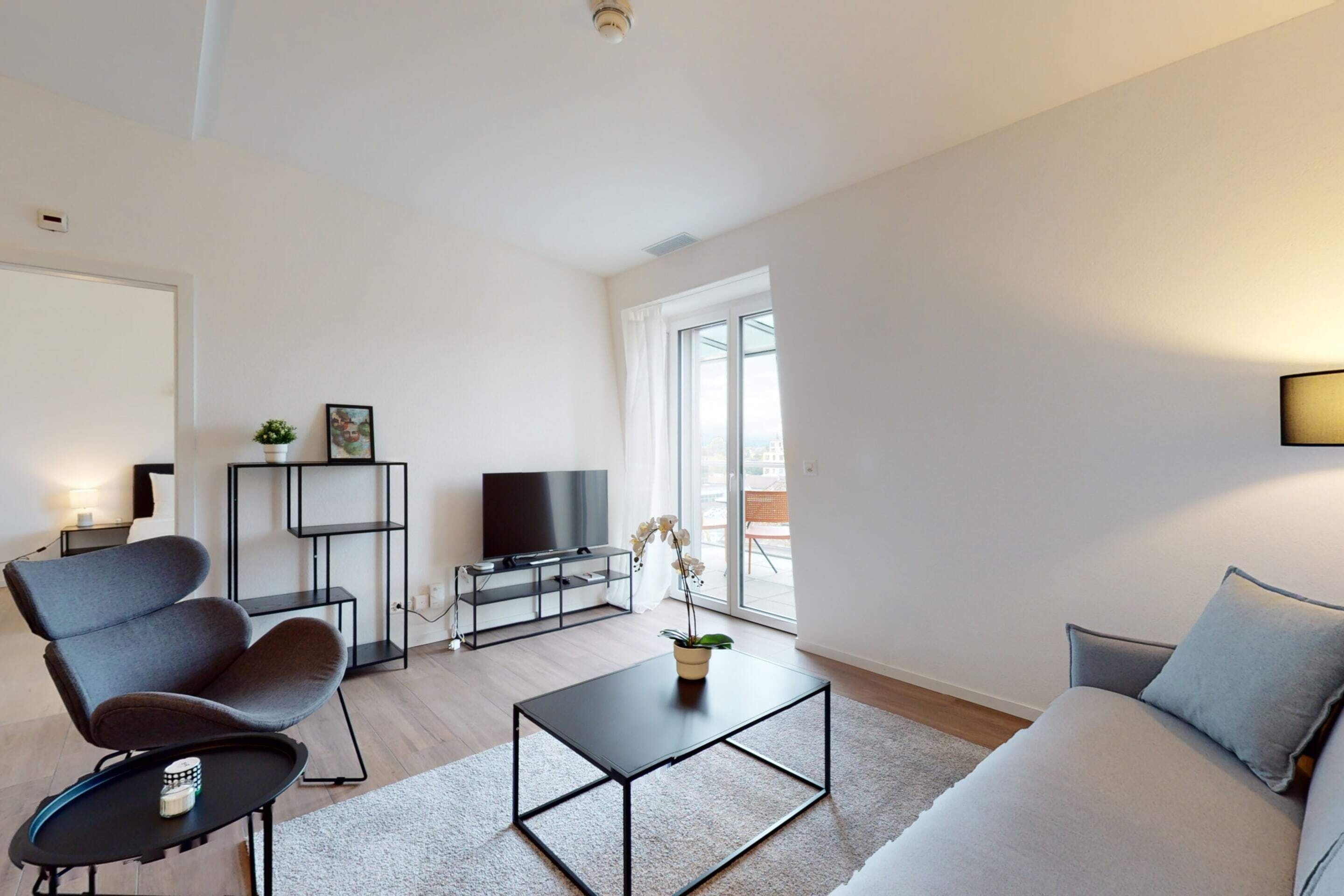 A modern living room with a grey sofa, a black coffee table, a grey armchair, a black TV stand, and a potted plant.