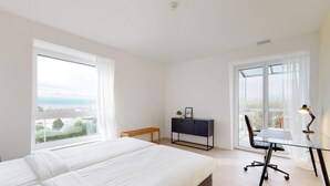 A bedroom with a bed, a desk, a chair, and a view of the city. - Lodges Hotel Morges (Morges)