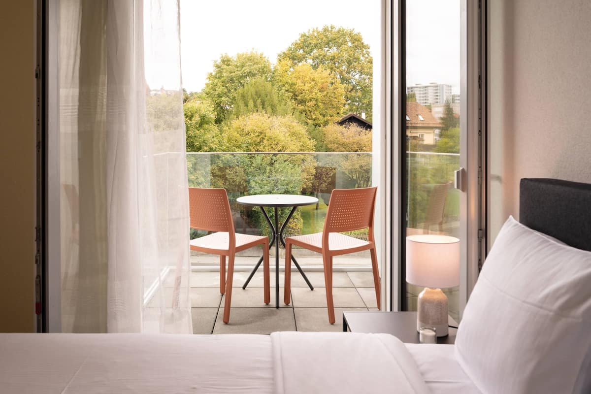 A hotel room with a balcony, a bed, a table with two chairs, and a lamp.