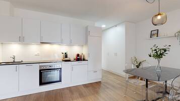 A modern kitchen with white cabinets, a built-in oven, and a dining area with a glass table and chairs.