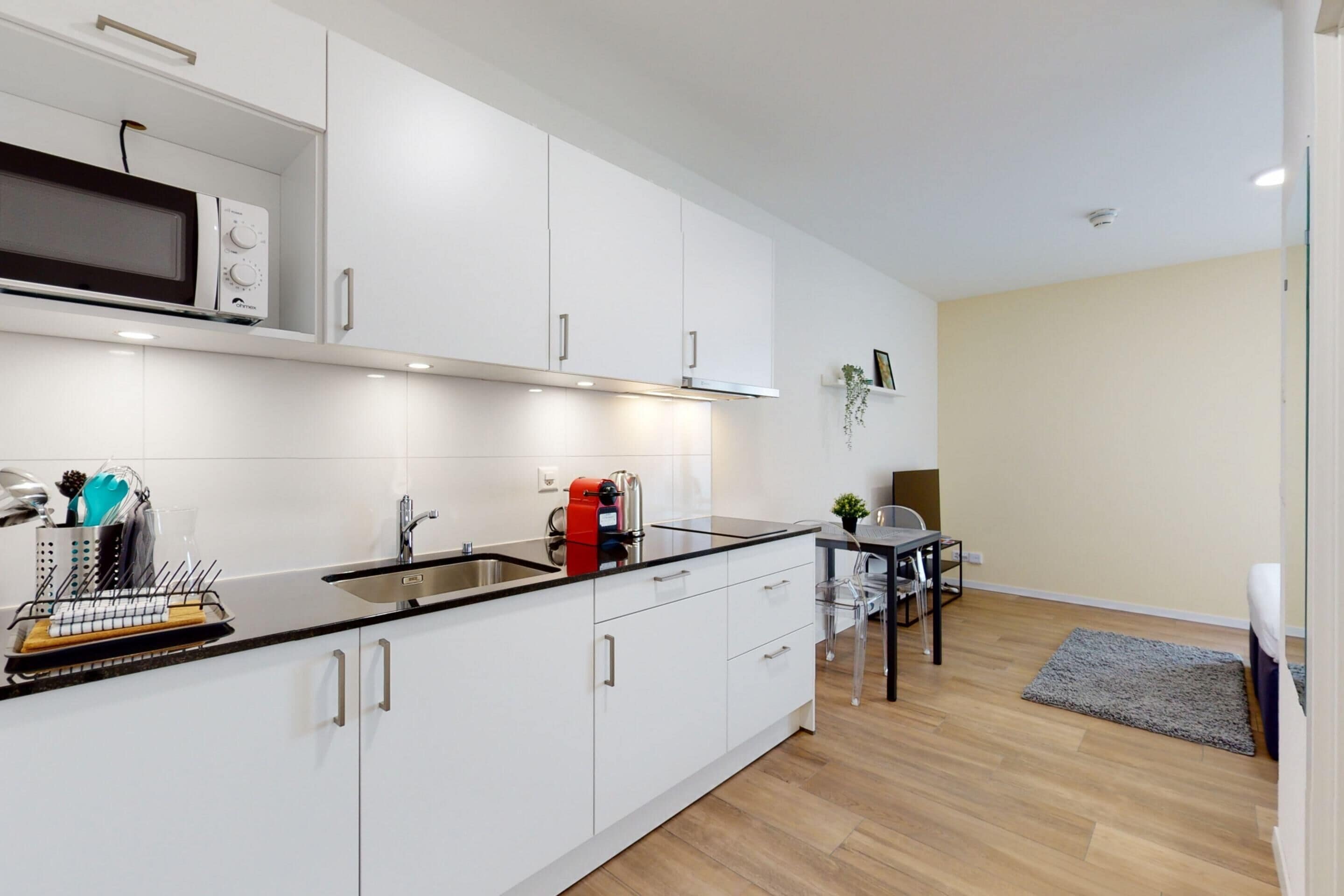 A modern kitchen with white cabinets, a black countertop, and a microwave. There is a coffee maker and a sink.