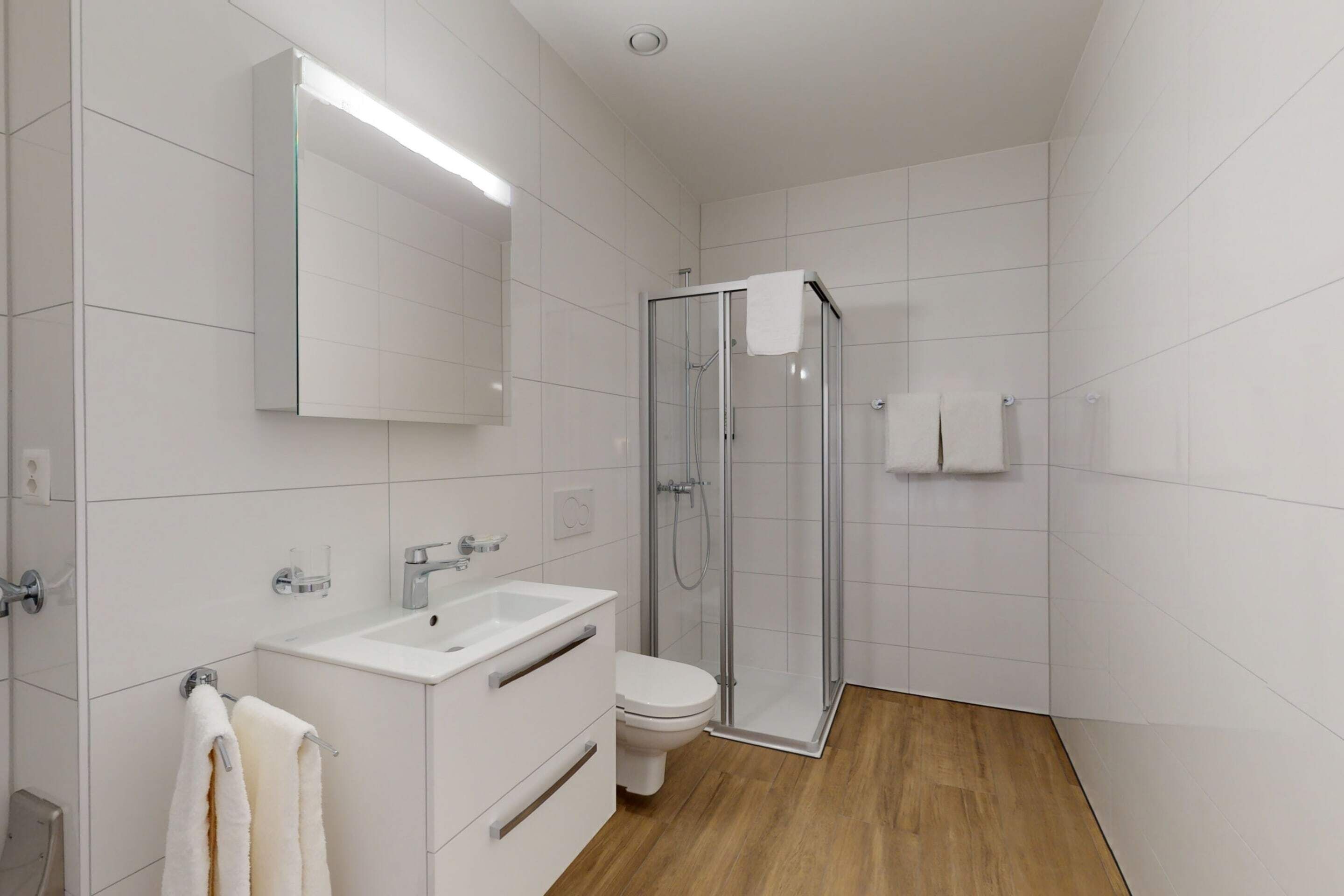 Un baño moderno con cabina de ducha de vidrio, un lavamanos blanco y un inodoro.