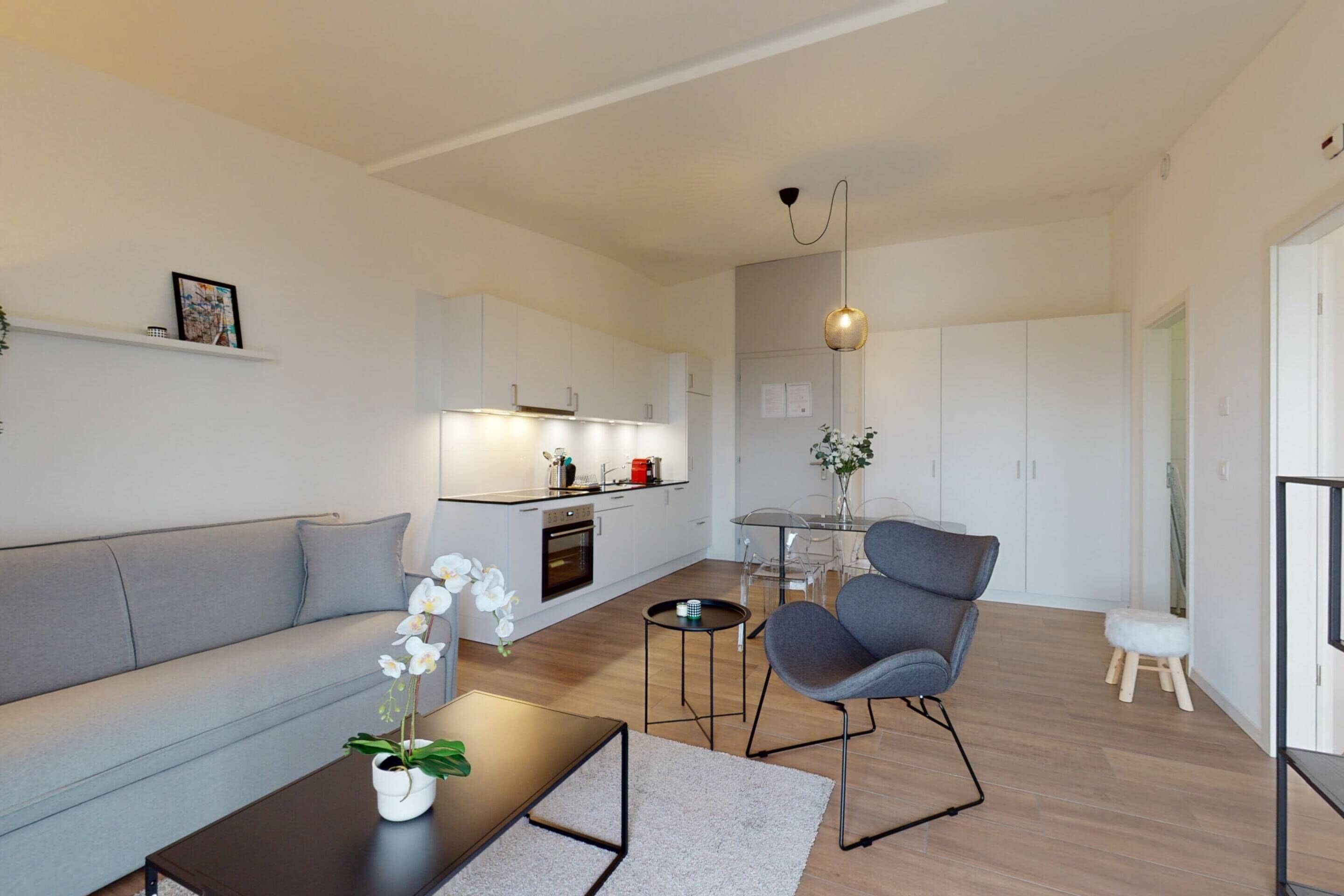 Una sala de estar moderna con un sofá gris, una mesa de centro con un jarrón de flores, un sillón gris y un taburete pequeño.