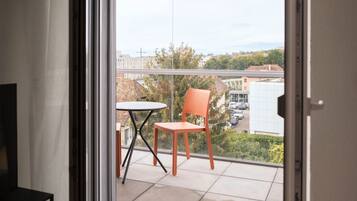 En balkon med et bord og to stole, der giver udsigt til bygninger og træer.