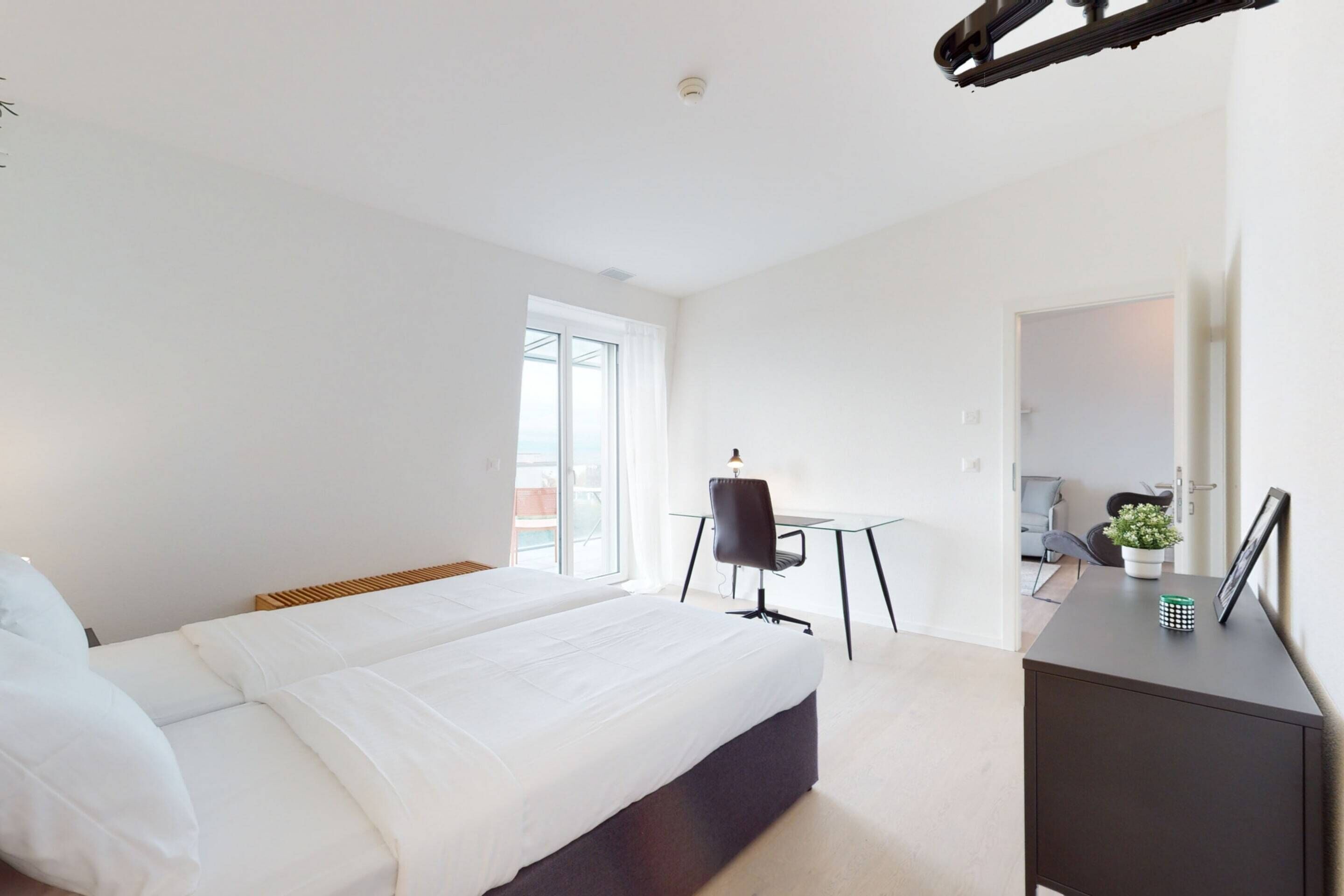 A modern hotel room with a large bed, a desk, and a chair.