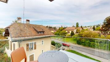 A balcony with a table and chairs, overlooking a street with houses and greenery.