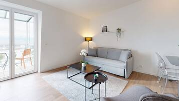 Un salon moderne avec un canapé, une table basse et une lampe. On aperçoit un balcon avec une chaise à travers les portes vitrées.