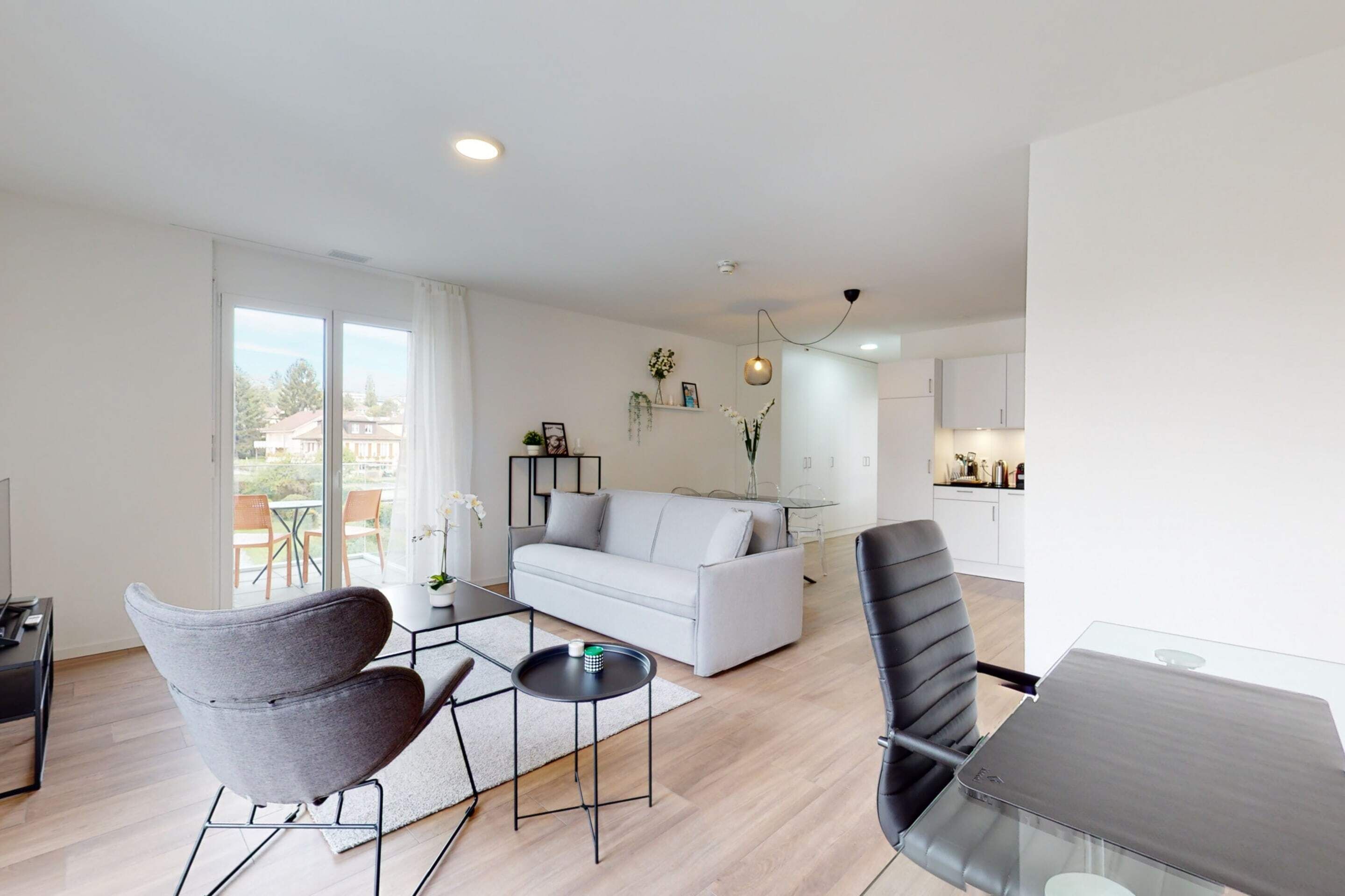 A modern living room with a sofa, a dining table, and a kitchen in the background.