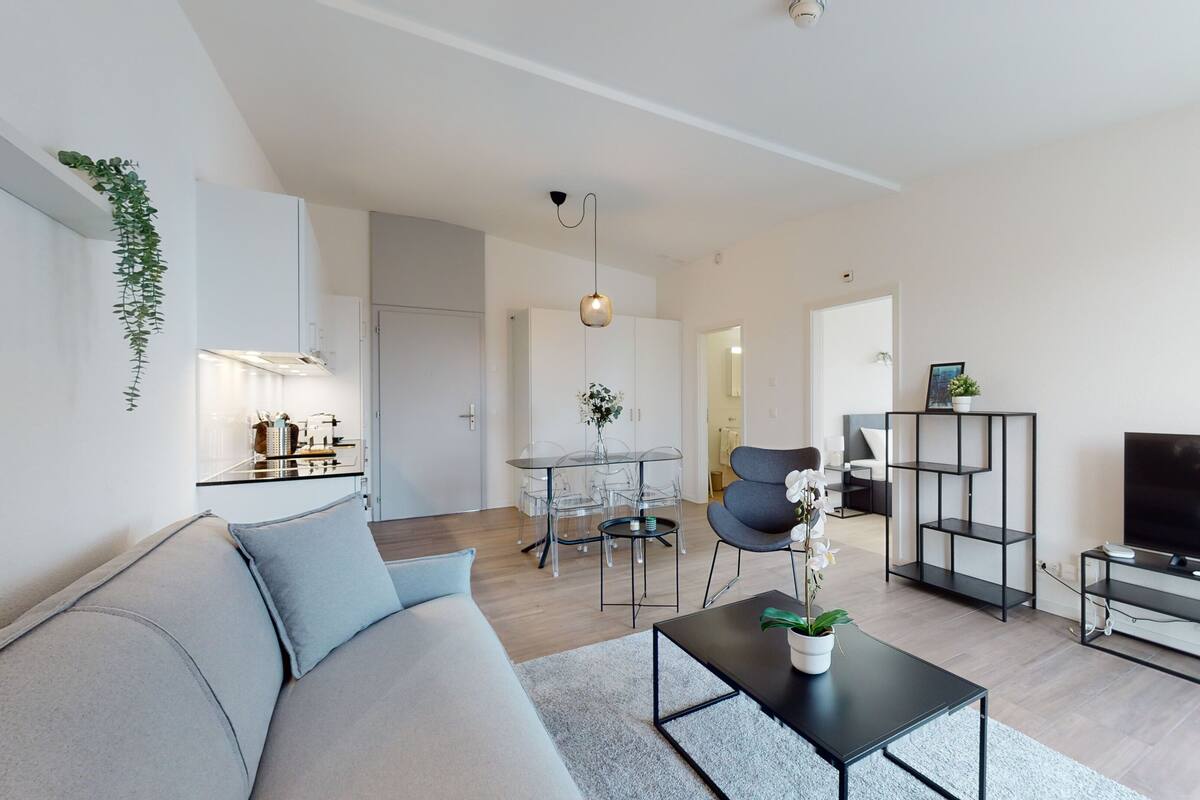 A modern living room with a sofa, coffee table, TV, and a dining area with chairs and a table.