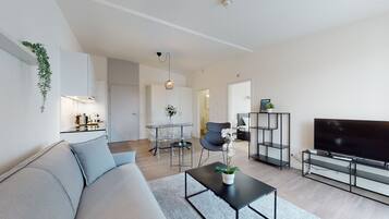 A modern living room with a sofa, coffee table, TV, and a dining area with chairs and a table.