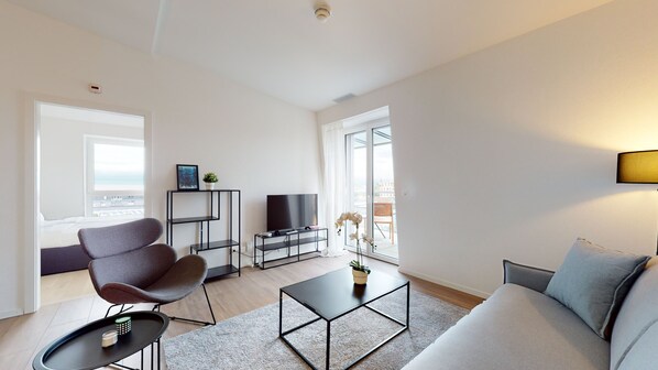 Una sala moderna con sofá, sillón, televisor y balcón con vistas.