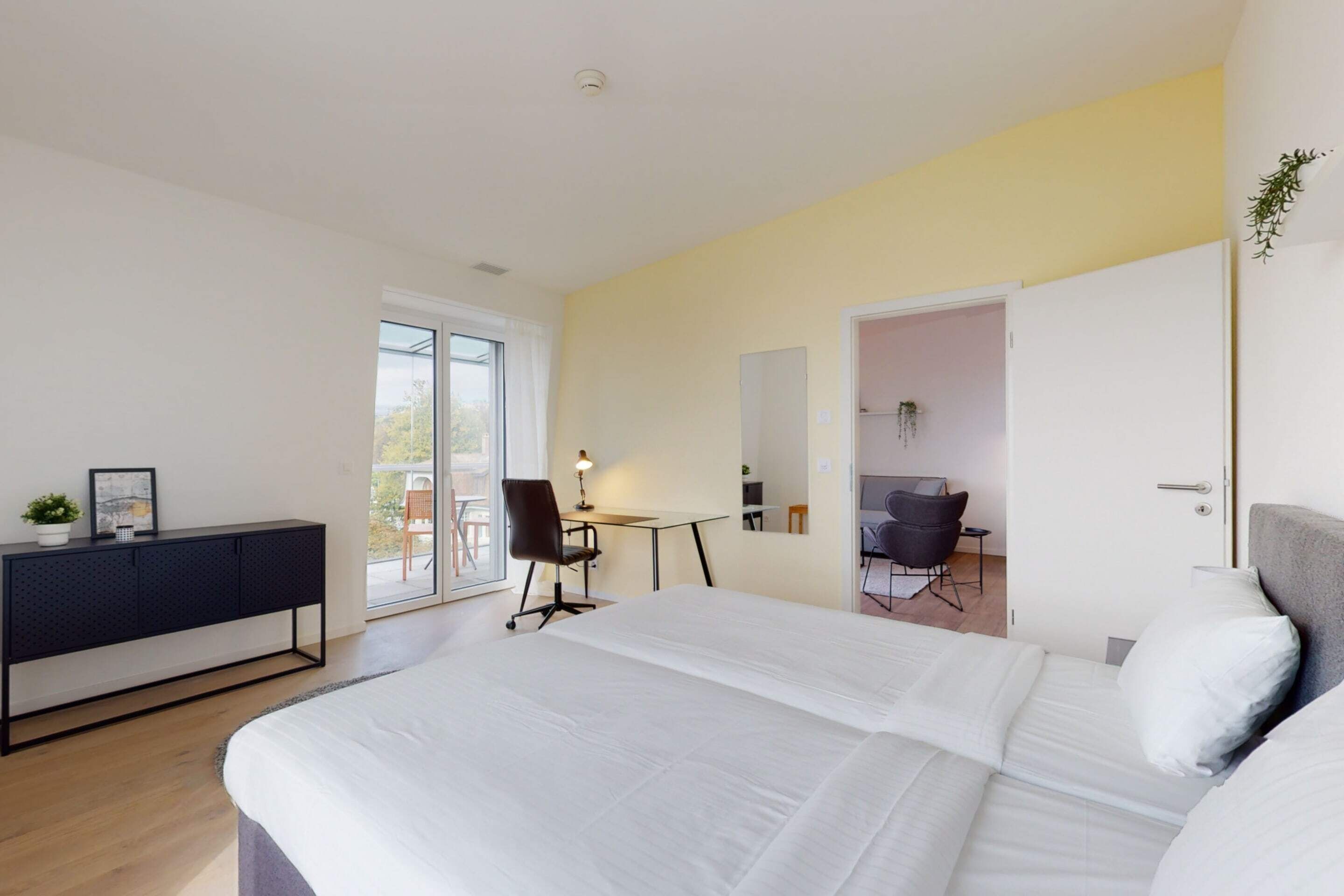 Een moderne hotelkamer met een groot bed, een bureau en een stoel. Er is een schuifglazen deur die leidt naar een balkon.