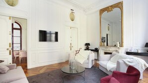 Un salón espacioso con una televisión grande, sofás blancos, un sillón rojo y una chimenea.