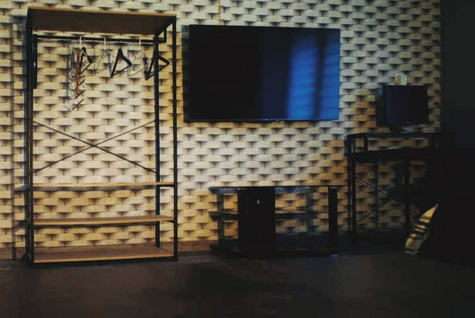 A room with a patterned wall, a TV mounted on the wall, and a metal rack with items hanging.