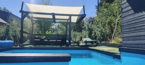 A swimming pool with a wooden deck and a canopy structure. - Studio G (Betting)