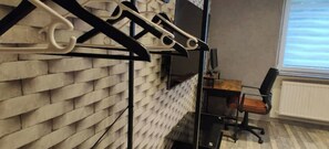 A room with a brick-patterned wall, a black metal shelf, a wooden desk, and a black office chair. - Studio G (Betting)