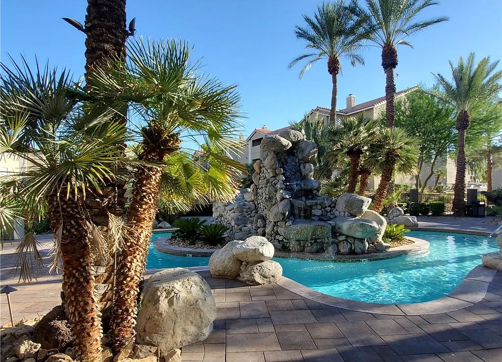A pool area with palm trees, a stone waterfall, and a clear blue pool.