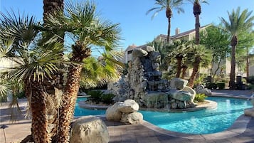 A pool area with palm trees, a stone waterfall, and a clear blue pool.