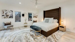 A modern bedroom with a large bed, a bench, a round mirror, and artwork on the walls. - Modern Luxury In The City at Havilah Estates (Atlanta)
