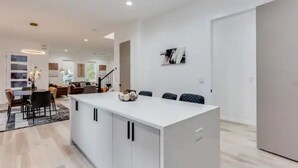 A modern kitchen with a central island, white cabinetry, and a dining area with a table and chairs. - Modern Luxury In The City at Havilah Estates (Atlanta)