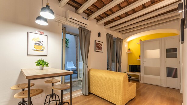 A cozy living area with a wooden ceiling, a yellow sofa, a wooden table with stools, and a small plant. - Casa Abbanniata a Ballarò by Wonderful Italy (Palermo)