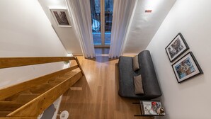 A modern apartment with a wooden staircase, a gray sofa, and a small shelf with items. - Casa Abbanniata a Ballarò by Wonderful Italy (Palermo)