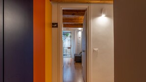 A hallway with a wooden ceiling, a white door, and a view into a room with a grey sofa. - Casa Abbanniata a Ballarò by Wonderful Italy (Palermo)